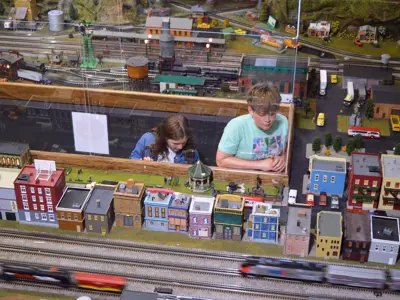 An overhead view of the NNYCRRM's O-gauge model train layout with kids watching model trains